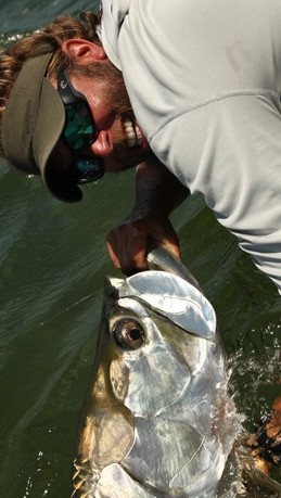 Capt. Mitchell Dugger holds a tarpon by the jaw and smiles for the camera.